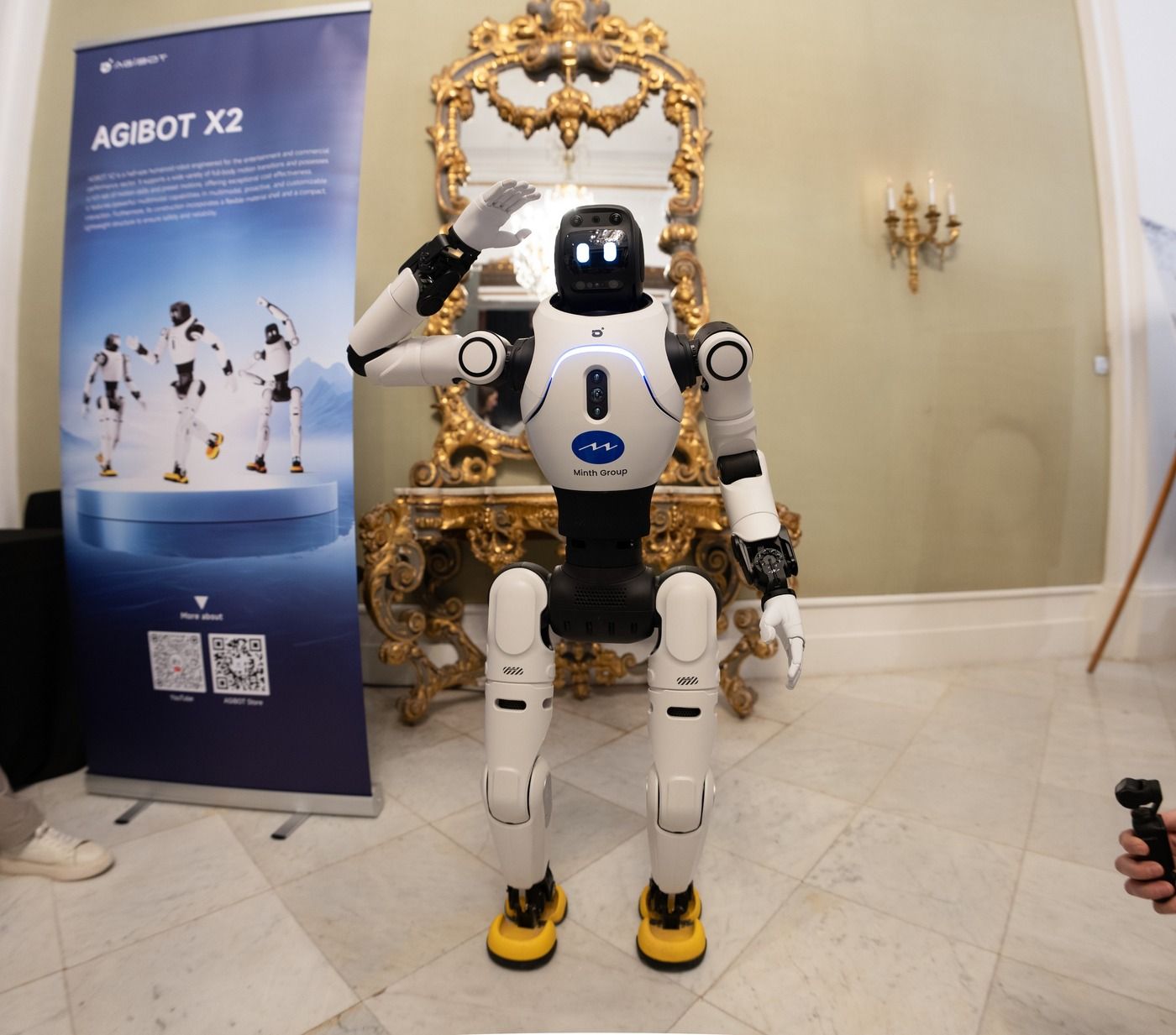 Zdjęcie robota humanoidalnego AgiBot X2 machającego ręką przed stoiskiem producenta podczas targów MWC Barcelona w marcu 2026 roku.